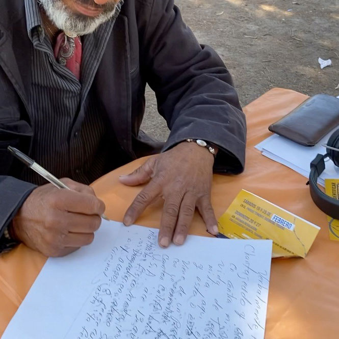 una persona mayor hace un guión sobre una hoja de papel, al lado hay unos audífonos