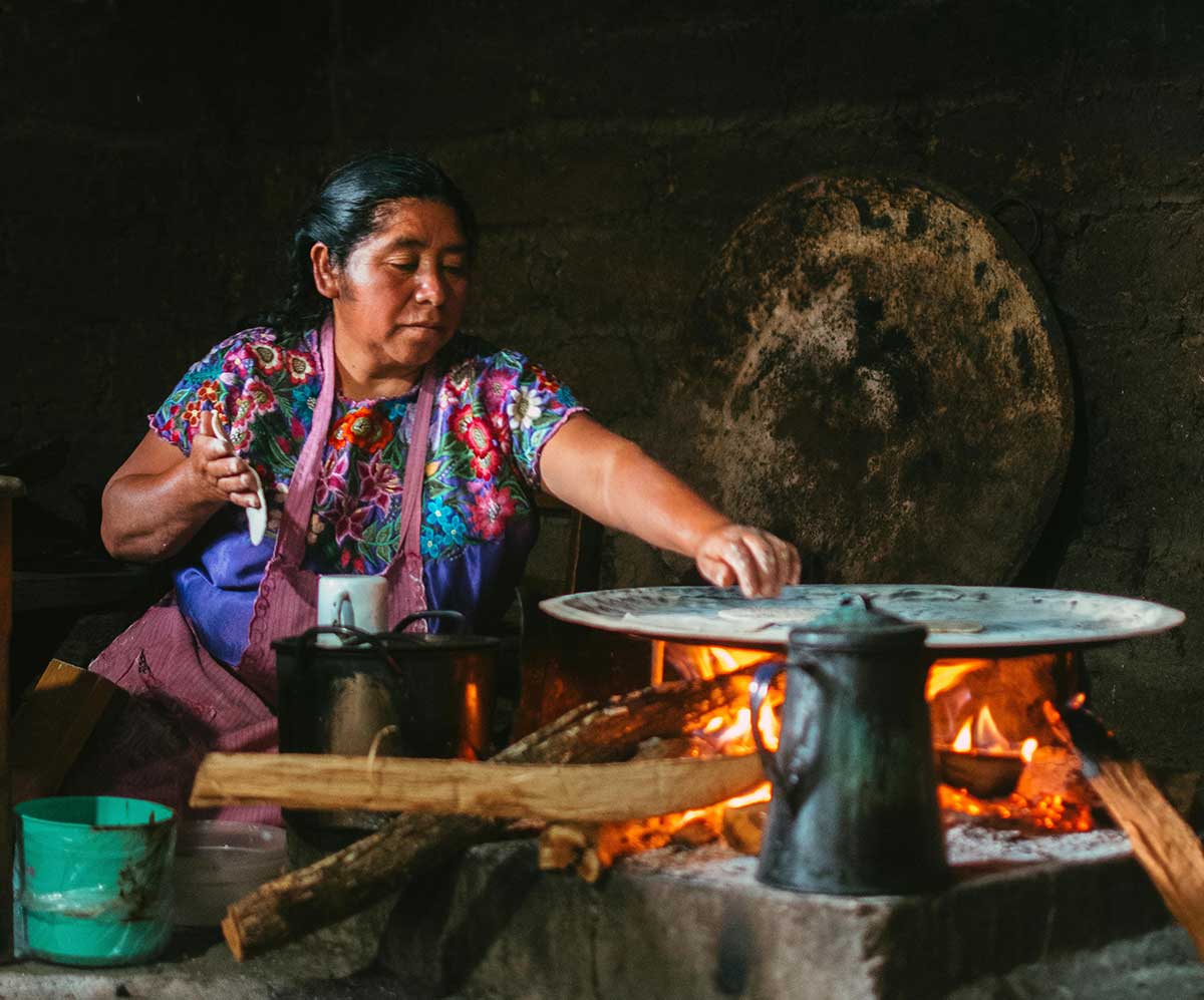 Una mujer indígena calienta una tortilla en un comal en el suelo